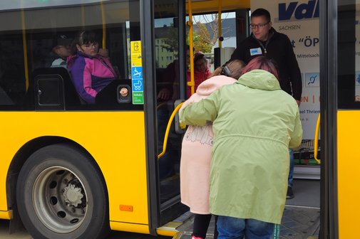zwei Frauen steigen über eine Rampe in einen Bus ein, eine davon am Rollator